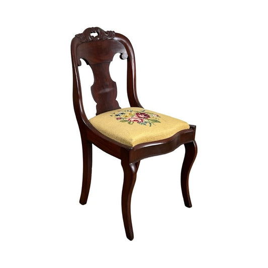 Antique American Empire Flame Mahogany Saber Leg Side Chair, mid-19th century, features a carved backrest and cushioned seat upholstered in yellow fabric with floral needlepoint embroidery. Brand: Unknown.