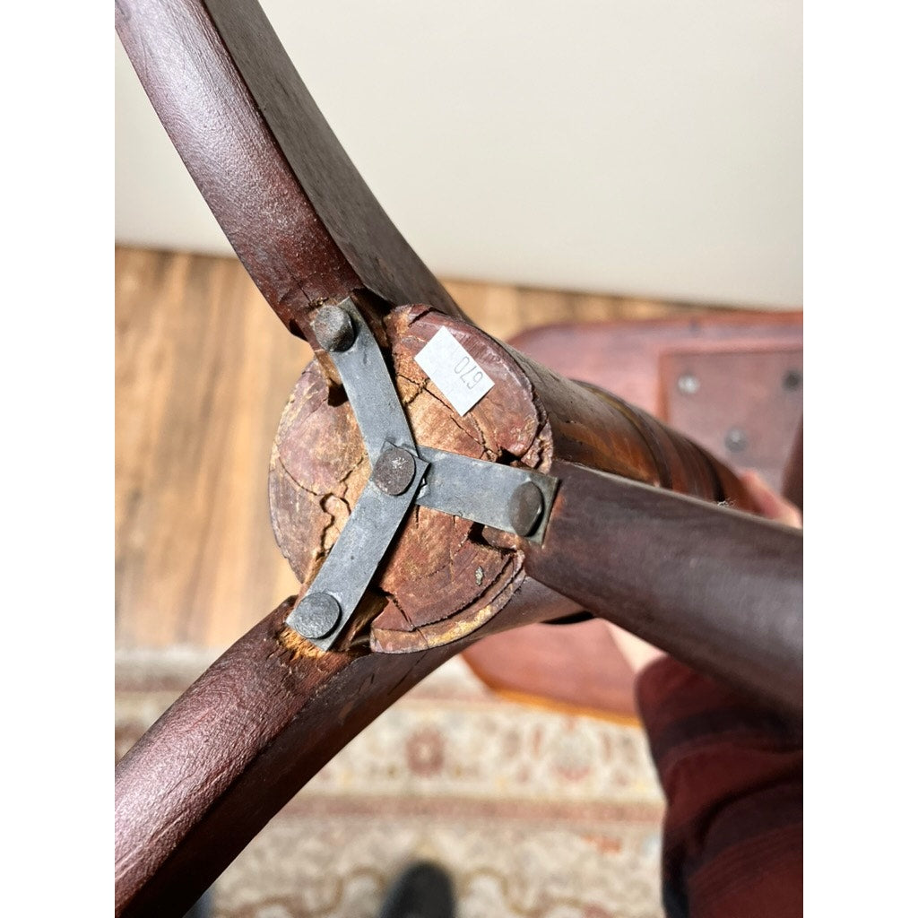 Close-up of the bottom of an Antique Federal Period Cherry Hepplewhite Candle Stand (mid 19th century) with cracked wood, metal braces, and a price tag, held above a rug on a wooden floor. Brand: None/Unknown.