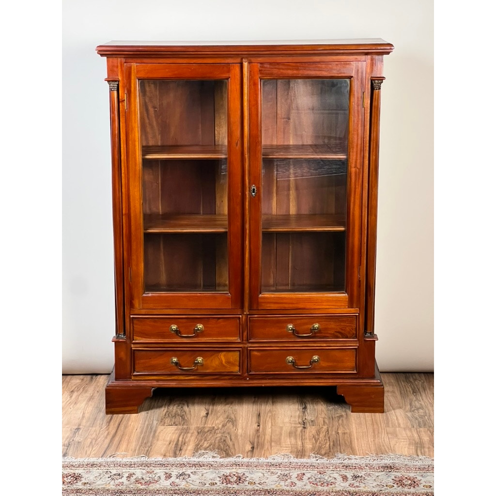 The Vintage Victorian Style Glass Door Mahogany Bookcase features two glass doors, four drawers with brass handles, and decorative columns. It stands on a wood floor with a patterned rug partially visible in front. Brand: Unknown.