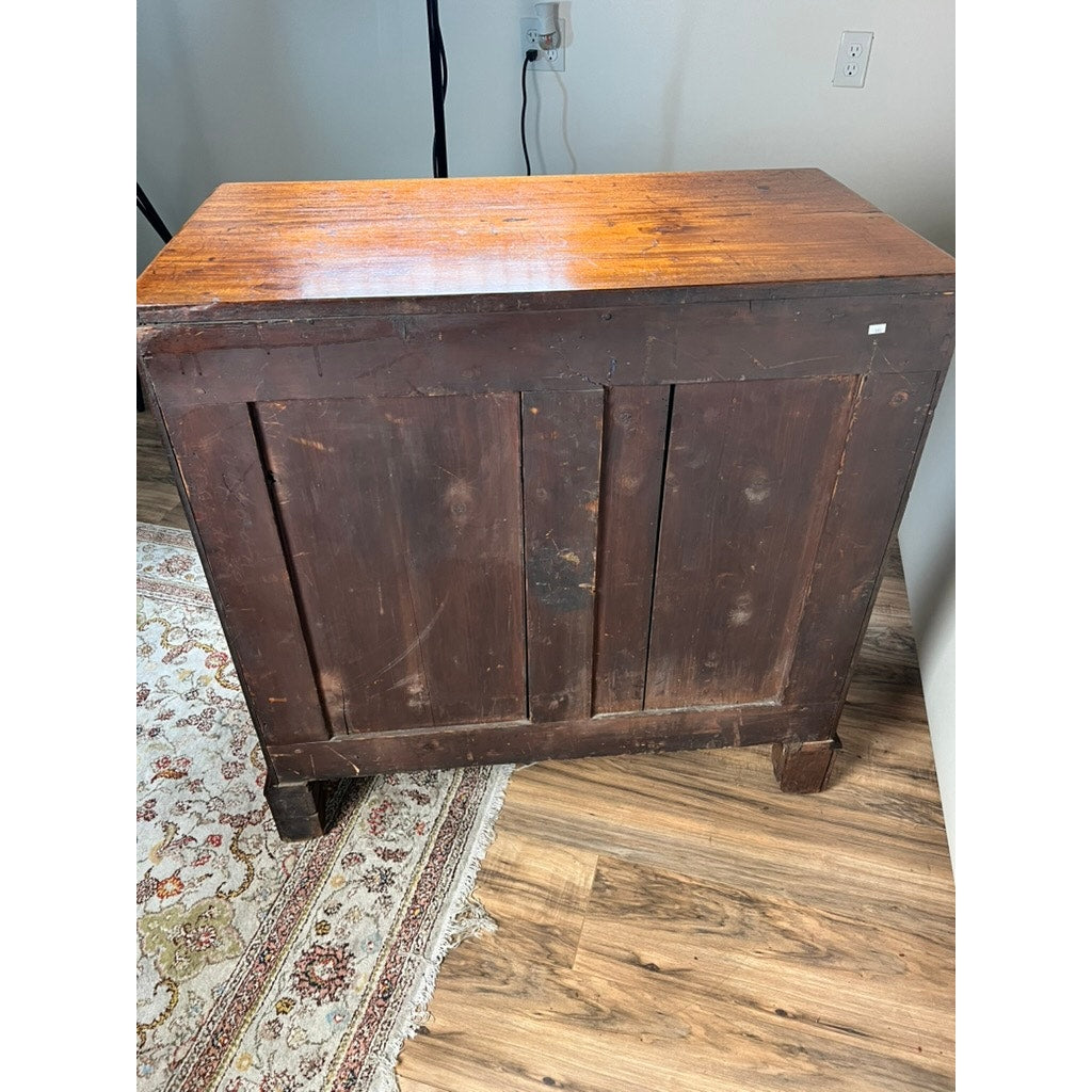 A Late Georgian English Mahogany Chest of Drawers, circa 1780–1810, with a timeworn dark finish, stands on a hardwood floor beside a patterned rug. Reminiscent of period furniture, the chest features two panel doors and displays visible scratches and marks that reflect its age and use.