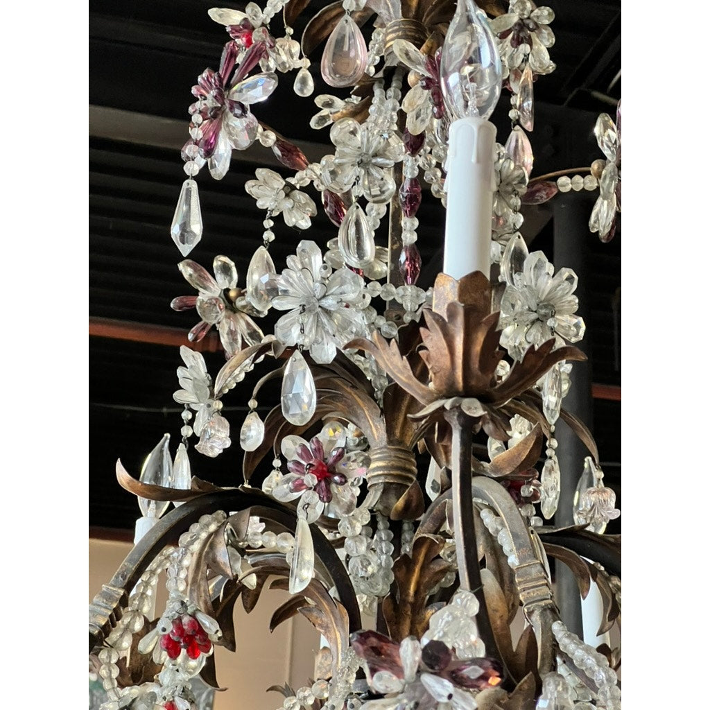 A close-up of an Antique Late 19th Century French Rococo Tole Amethyst and Crystal Ten Light Chandelier, featuring candle-style bulbs, gold-toned metalwork, and floral designs with clear and amethyst prisms against a beamed ceiling.