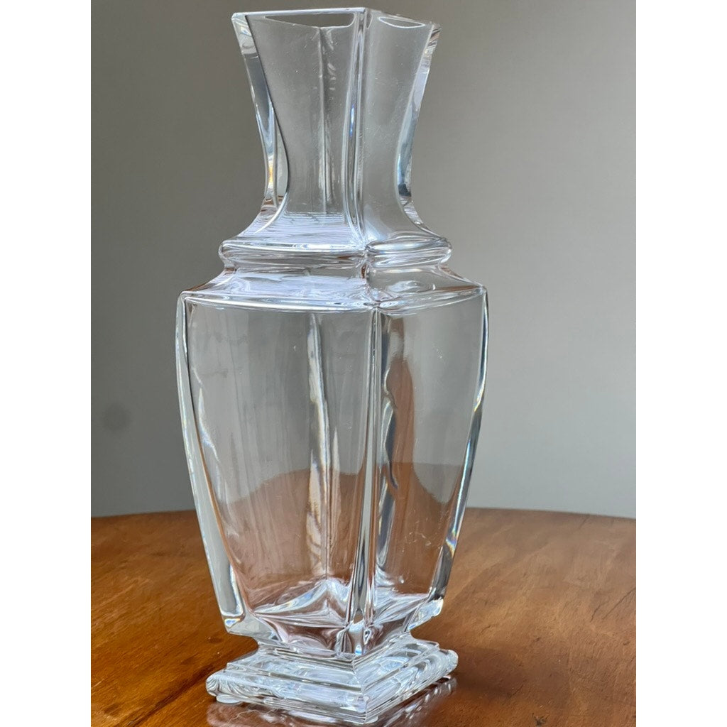 The Vintage Baccarat Crystal Pearl Vase by Baccarat, featuring a clear, faceted design with geometric angles, stands on a wooden surface against a neutral background.
