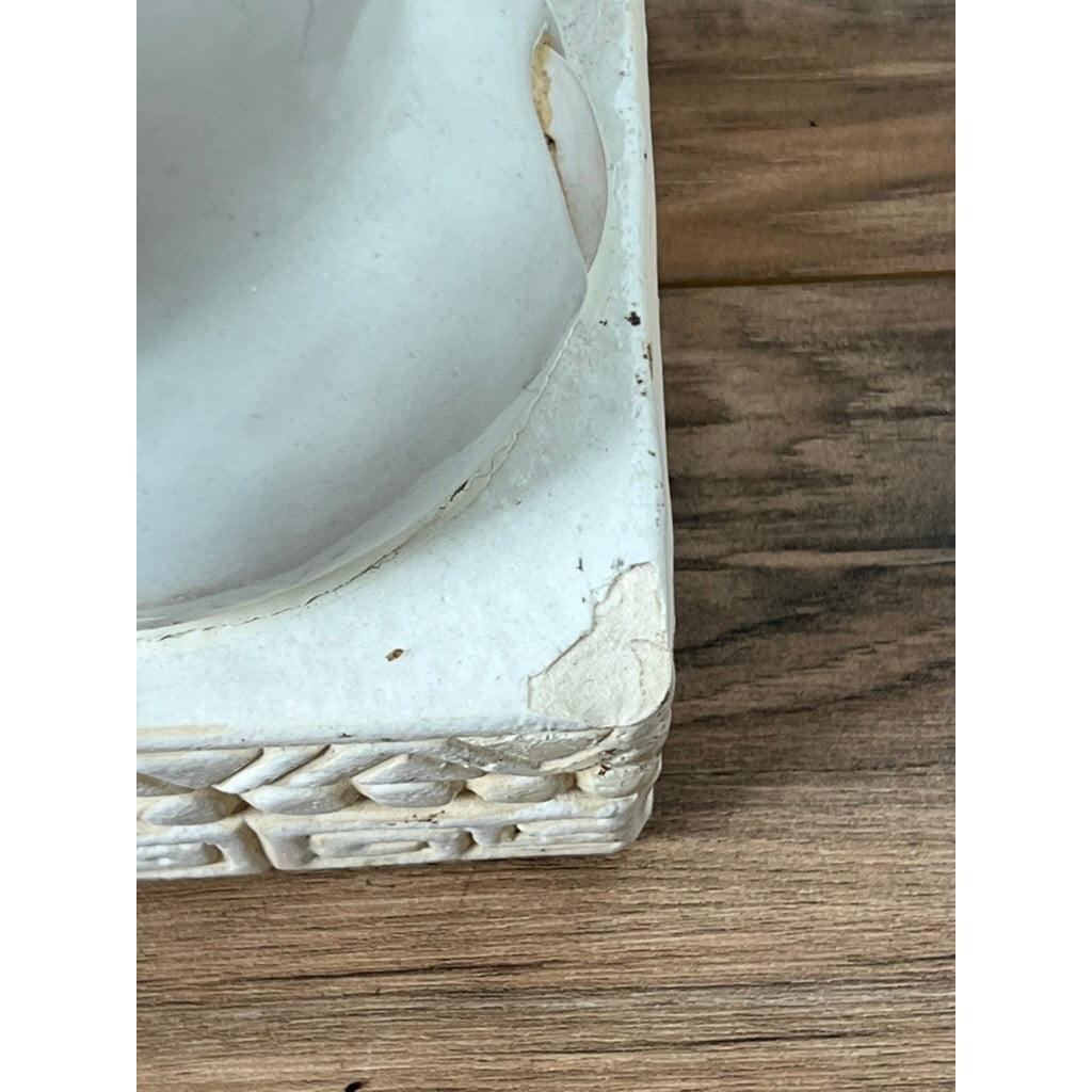 Close-up of a chipped Vintage Pair White on White Glazed Hollywood Regency Style Elephant Garden Seat, with a textured edge and visible damage on the bottom right corner, resting on wood and exuding classic vintage charm. Brand unknown.
