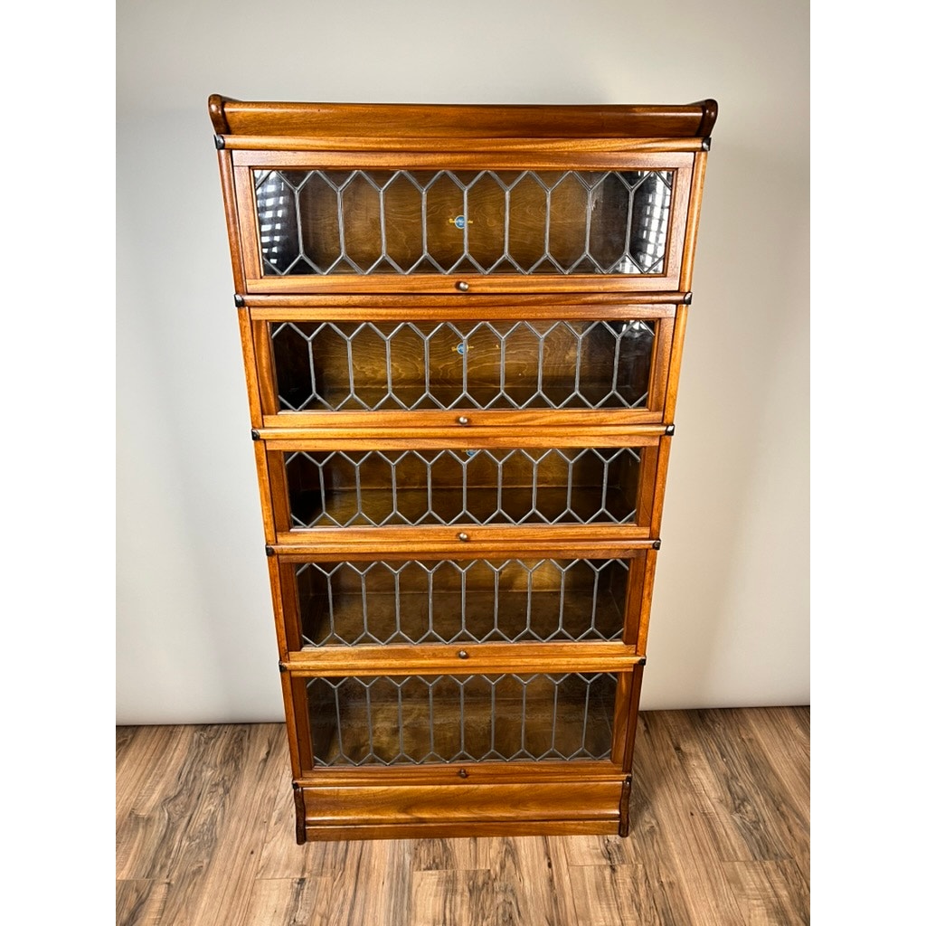 The Globe Wernicke Vintage Leaded Glass Five Stack Barrister Bookcase features five glass-fronted shelves with a diamond lattice, standing on a wood floor against a plain light-colored wall.