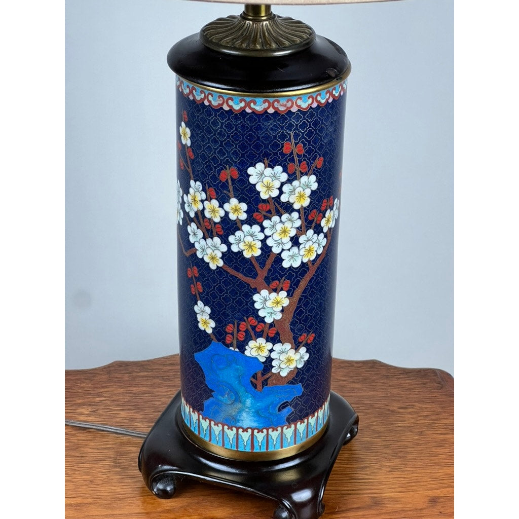 The Knob Creek Vintage Japanese Cloisonné Cylinder Table Lamp features a blue base with white and red cherry blossom motifs, blue accents, and sits on a dark wooden stand for an elegant decorative touch.