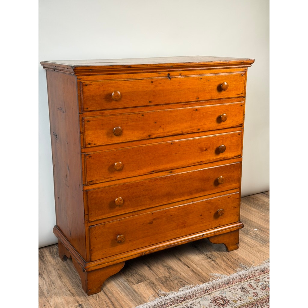 A Late 18th Century New England Pine Two-Drawer Blanket Chest by Pearl City Antiques, dating from circa 1780–1810, stands on a wooden floor near a patterned rug against a plain white wall.