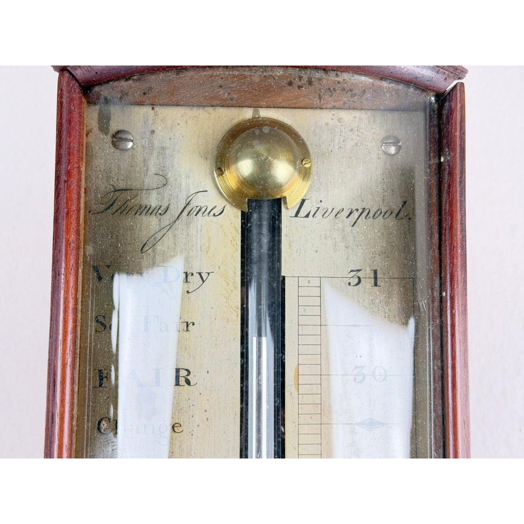 Close-up of an English Regency Mahogany Stick Barometer by Thomas Jones, Liverpool, c. 1820, featuring a mahogany body, brass top, and a glass-covered gauge labeled with weather conditions and numbers from 30 to 31.