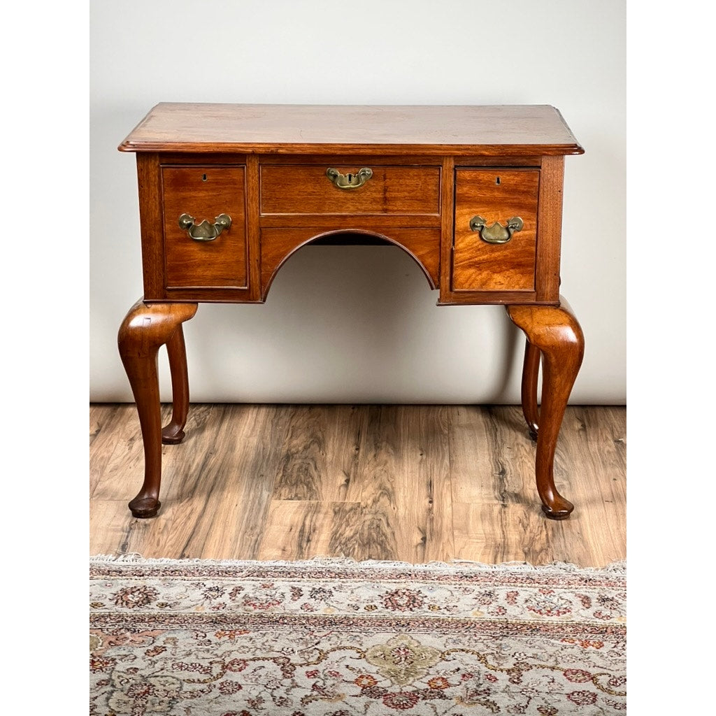 An Antique George III Queen Anne Mahogany Lowboy from the late 18th century with three drawers and cabriole legs stands on a wood floor, with part of a patterned rug visible in the foreground.