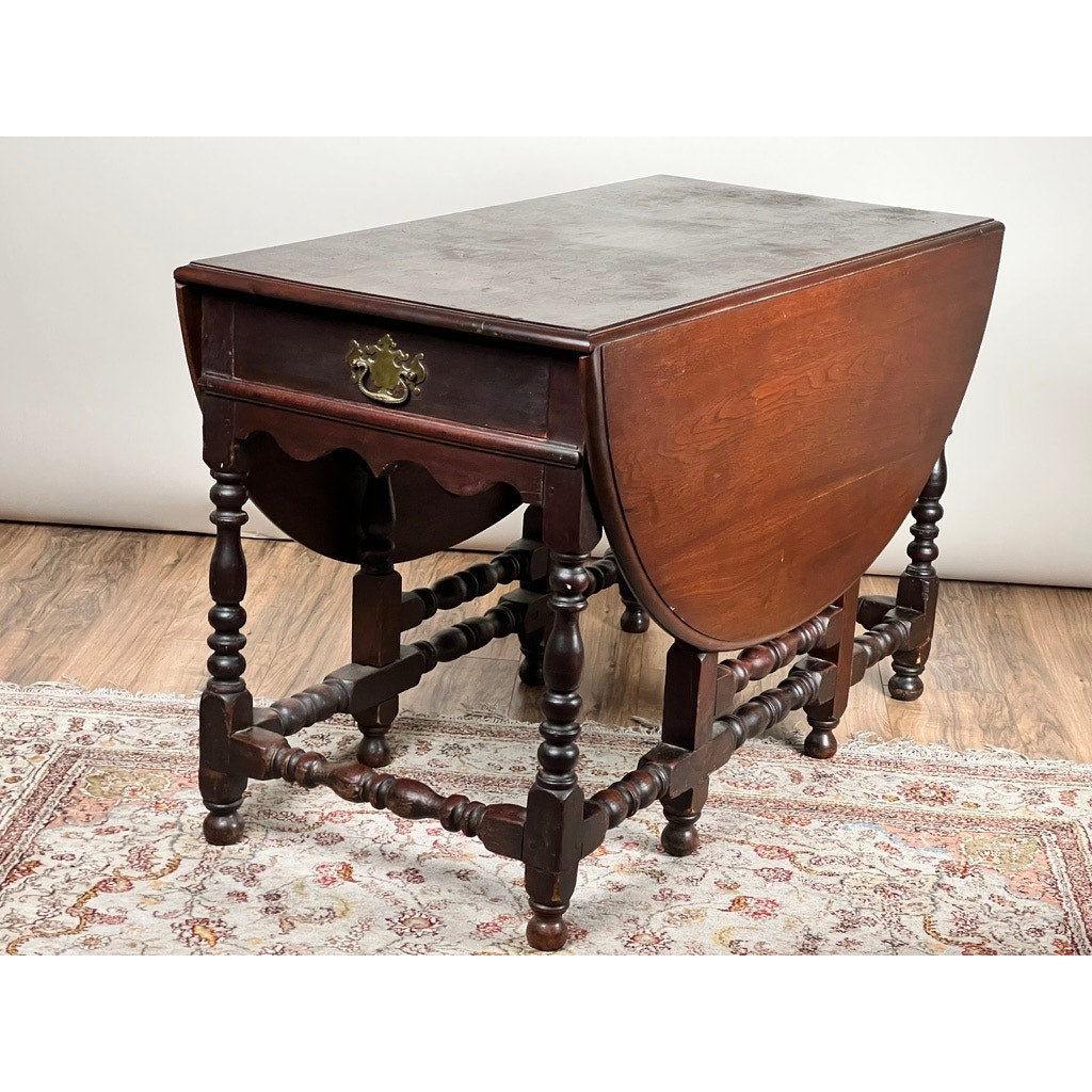 Antique English William & Mary walnut one drawer gateleg dining table, early 18th century, with turned legs and ornate stretcher supports, displayed on a patterned rug over a wooden floor. Brand unknown.