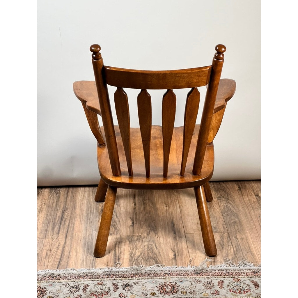 The Vintage Herman DeVries for Cushman No. 5-82 Rock Maple Easy Chair by Cushman features a spindle back and angled legs, set on a wood floor with part of a patterned rug below and a plain light-colored wall in the background.