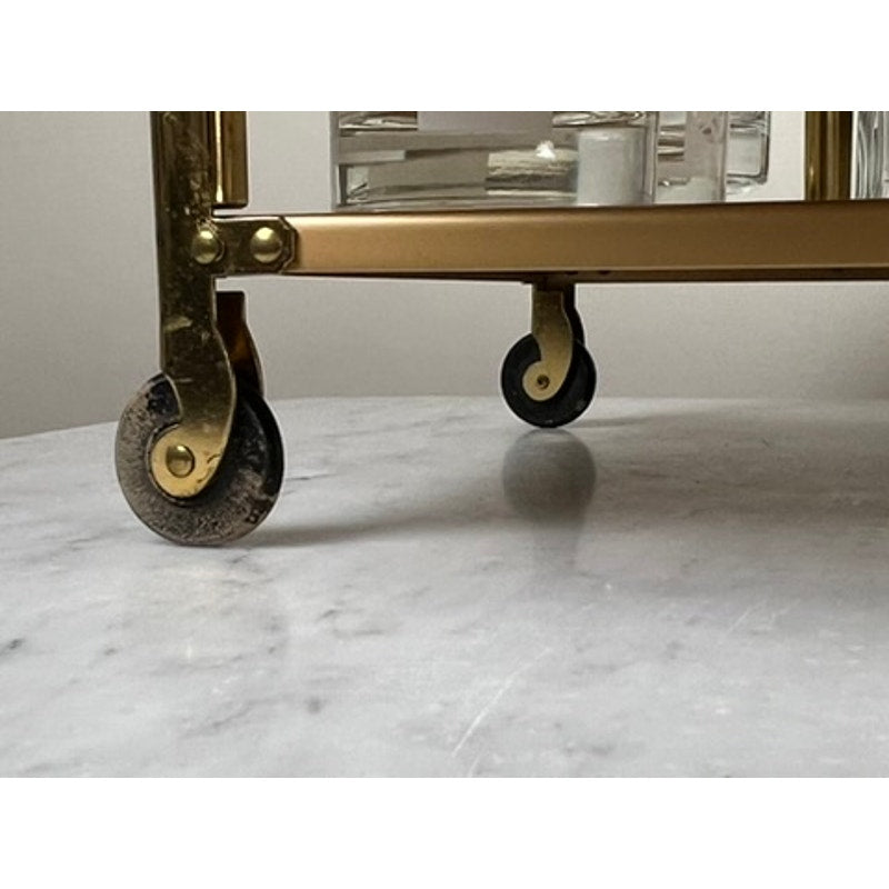 Close-up of two small black wheels on the gold frame of a Vintage Mid Century Modern Bar Caddy (c. 1960s) resting on white marble, with glassware visible above. Brand is none or unknown.