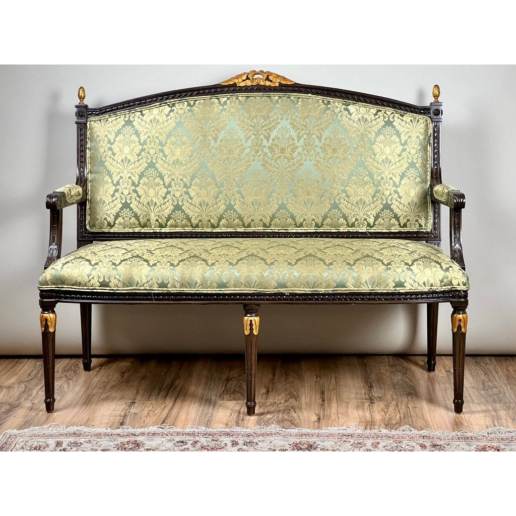 A Vintage Louis XVI Style Settee in green damask upholstery sits against a plain light wall on a wooden floor, with part of a rug visible in the foreground.
