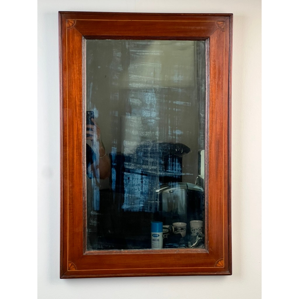 An American Federal Mahogany Wall Mirror with fan inlay and its original hand silvered glass, circa 1810–1825, features classic antique lines and a wooden frame. Its cloudy, streaked surface reflects part of a room, a person holding a phone, and objects on the shelf below. Brand: unknown.