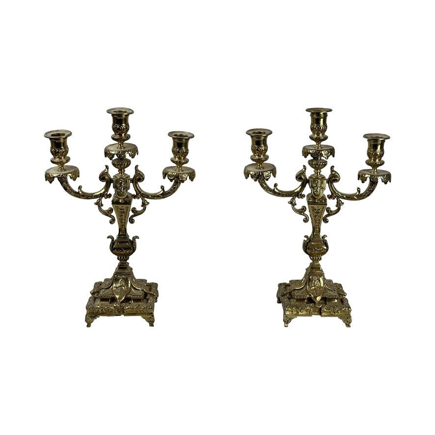 Two ornate brass candelabras on a white background
