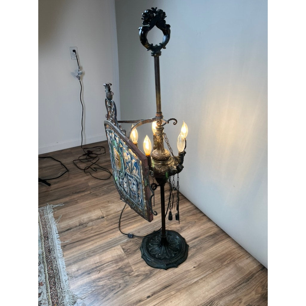 An Antique Five Burner Lucerne Whale Oil Lamp with Napoleon I Fireplace Screen Shade stands on wood flooring near a white wall and patterned rug, featuring ornate metalwork, exposed burners, and a colorful detailed side panel. Brand is unknown.