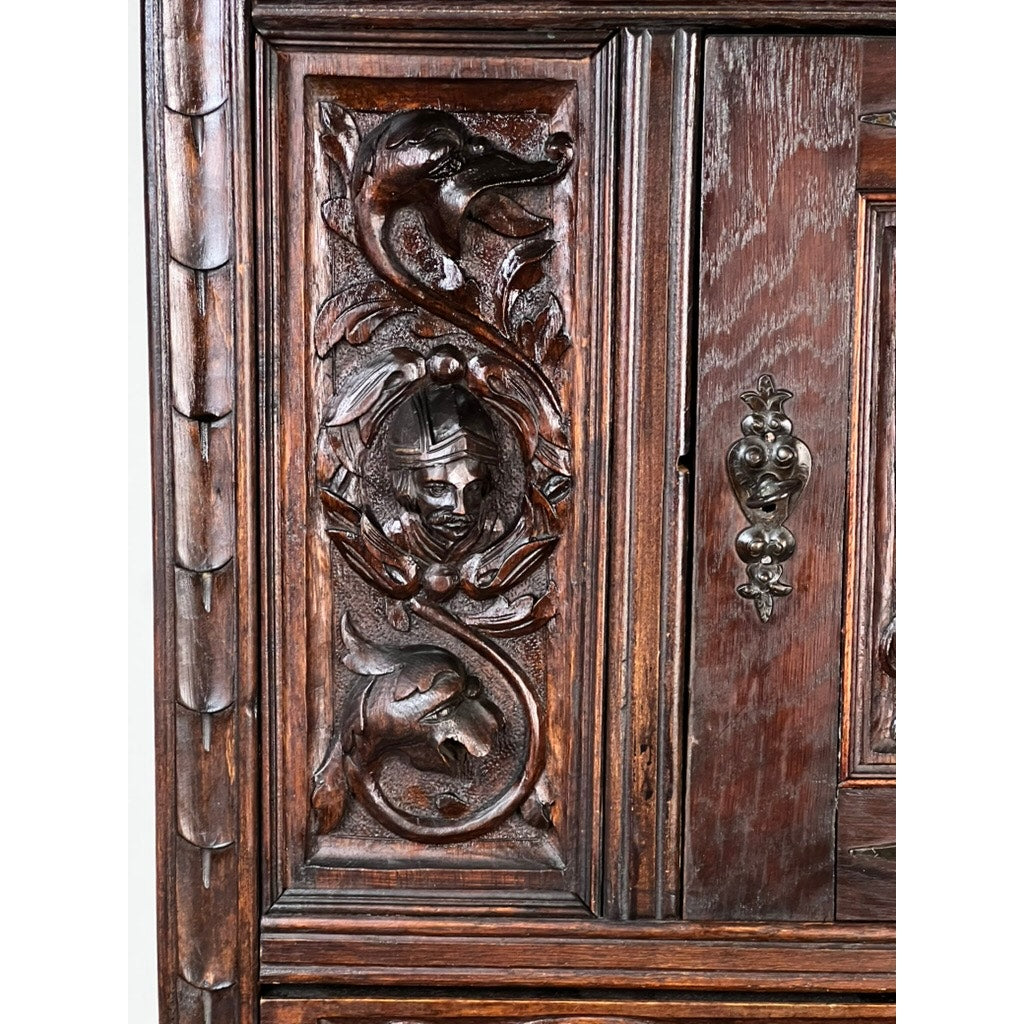 Close-up of an Antique 19th-Century French Breton-Style Carved Oak Cabinet, featuring deeply carved knights with ornate dragons, a helmeted head, intricate foliage, and a metal handle. Brand: None/Unknown.