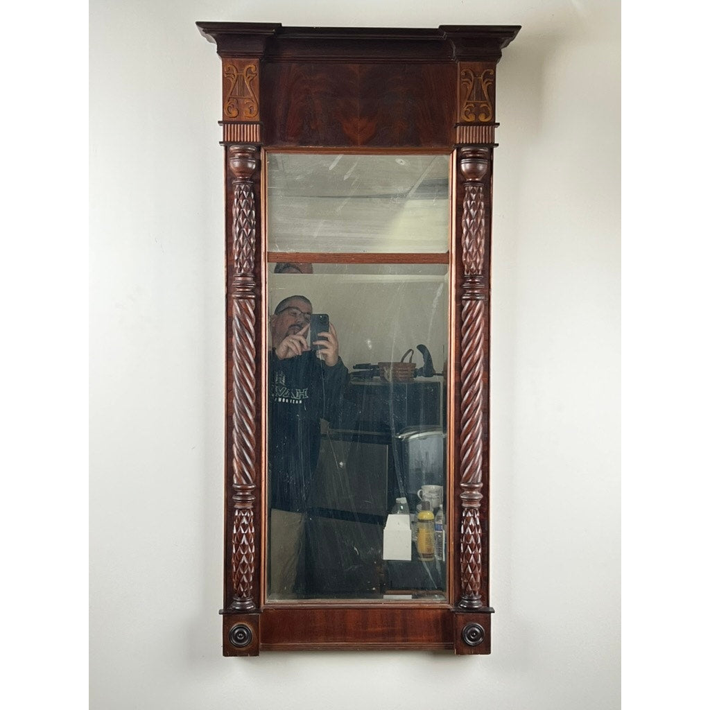 An Antique American Empire Mahogany Pier Mirror c. 1840, rectangular with ornate carved details, reflects a person taking a photo along with furniture and various household items in the background.