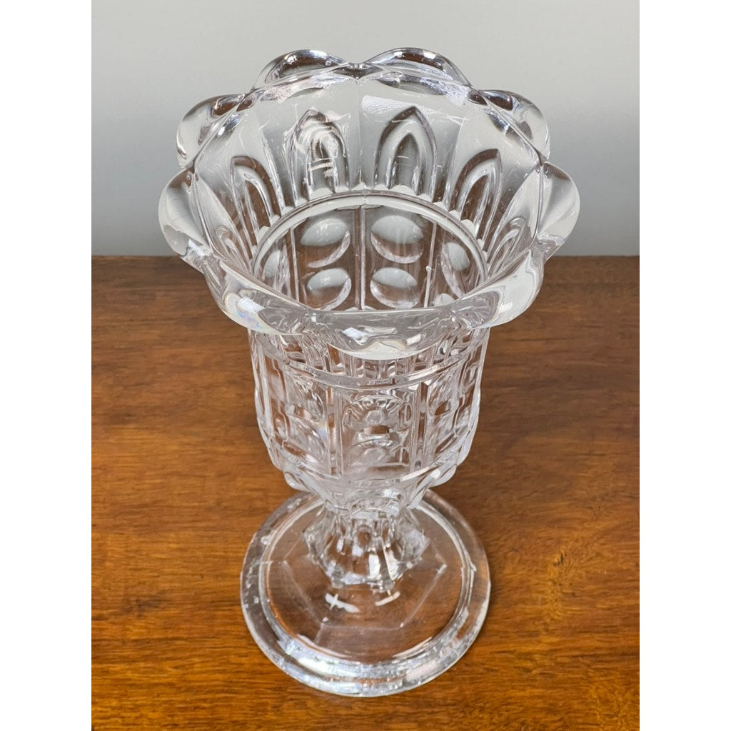 The Antique Boston & Sandwich Glass Co. Gothic Arch Pressed Glass Celery Vase (c. 1860–1880) by Sandwich Glass features a wide mouth, scalloped rim, geometric Gothic Arch patterns, narrow stem, and round base on a wooden surface.