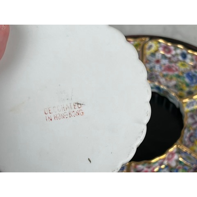 A close-up of a Vintage Chinese Canton Sweet Meat Set with Case (early 20th century) shows the underside of a white porcelain plate marked "DECORATED IN HONG KONG," with a colorful famille rose floral dish visible in the background.