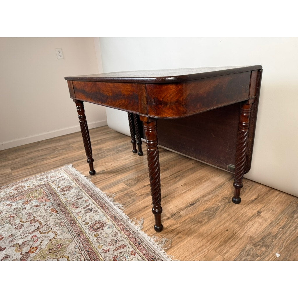 An American Classical Mahogany Single Drop-Leaf Table with Spiral-Twist Legs, c. 1830–1845, from Pearl City Antiques is placed on a wood floor near a decorative patterned rug, against a plain white wall.