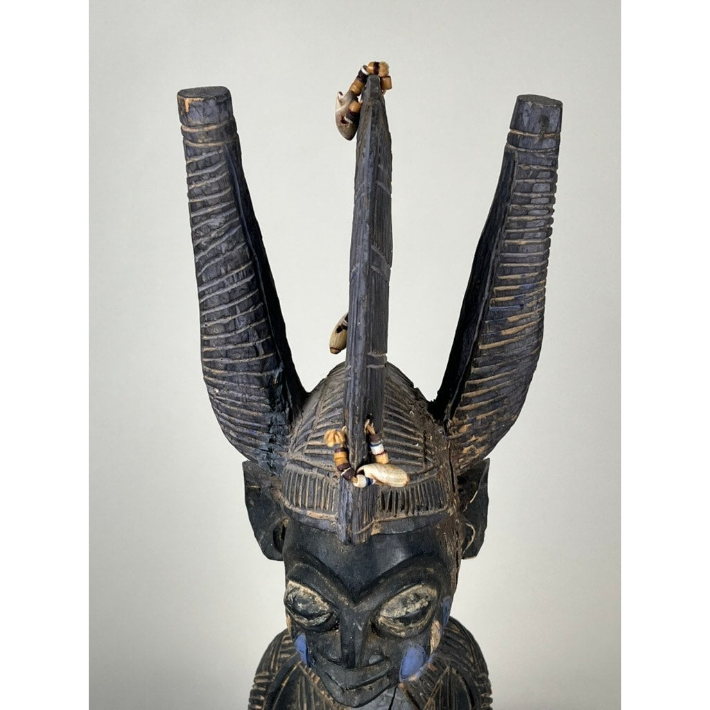 Antique Igbo Ikenga Shrine Figure, probably from Nigeria; a carved wooden head with tall curved horns, decorative shells, intricate patterns, and blue markings—an impressive example of traditional Igbo artistry. Brand: None/Unknown. Plain neutral background.
