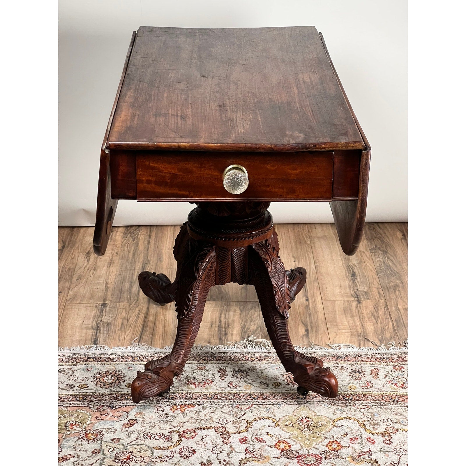 Antique American Empire Drop Leaf Table c. 1840, featuring great eagle carved feet and central drawer, displayed on a decorative rug with a white wall background. Brand: None/Unknown.