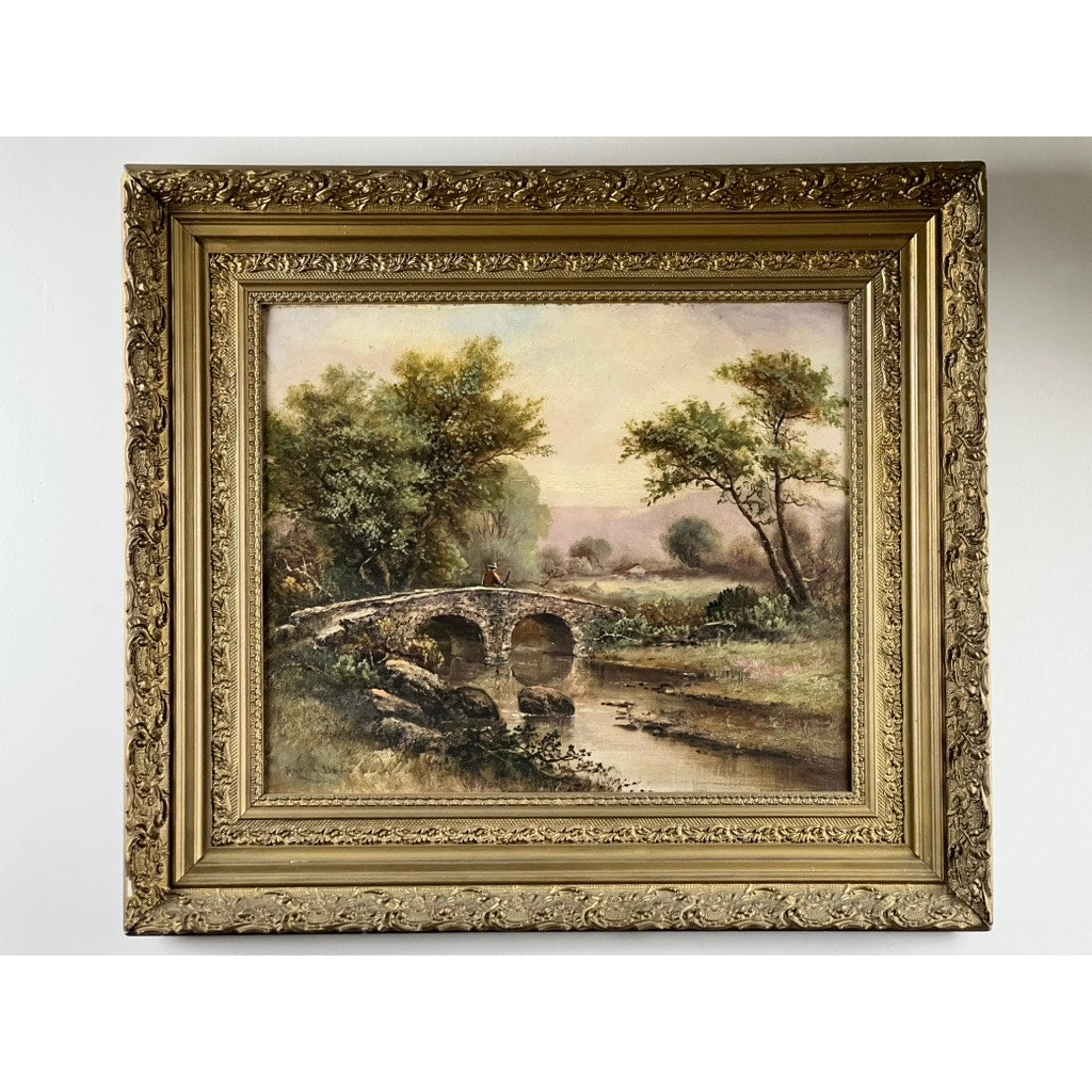 Antique early 20th century oil on canvas painting “Spectacle Bridge,” signed Arthur Davis lower left, features a stone bridge over a river and lush greenery in soft pastels under a hazy sky, set in an ornate gold frame with intricate patterns.