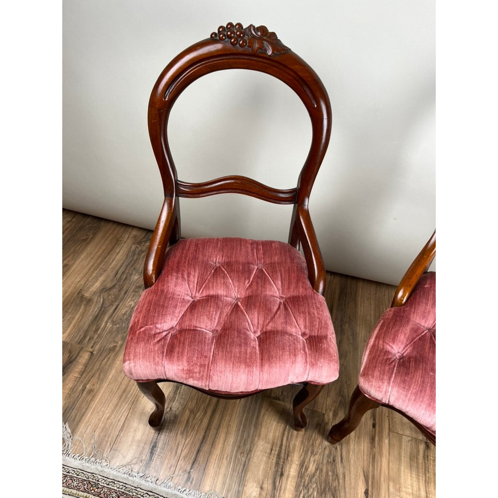 An Antique Pair of Victorian Walnut Balloon Back Tufted Side Chairs (c. Late 19th Century) with pink velvet seats is shown on a wooden floor near a white wall; only part of the second chair is visible. Brand: Unknown.