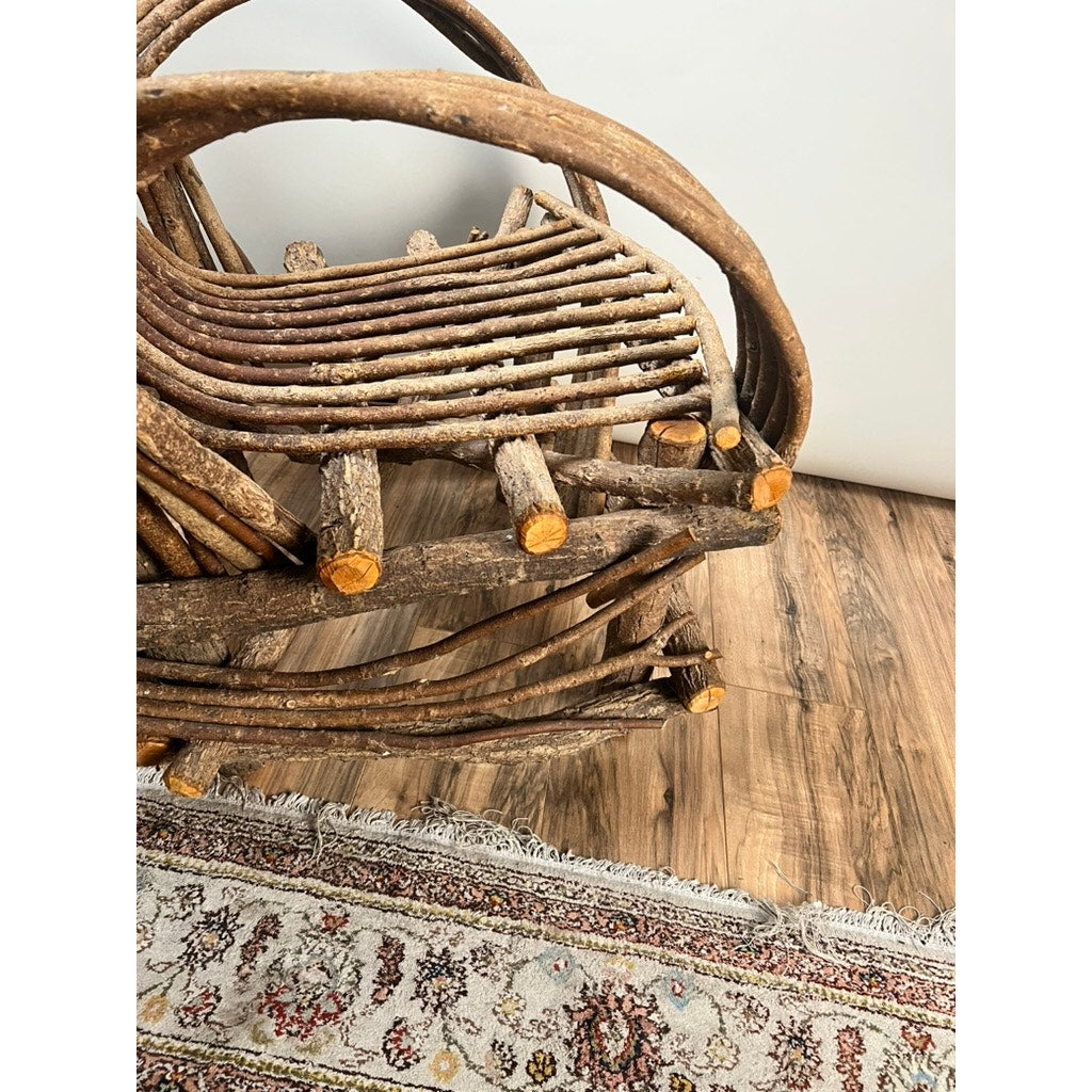 A close-up of a Vintage Adirondack Bent Willow Arm Chair, crafted from curved branches, sits on a wooden floor beside a patterned fringed rug. Brand: None/Unknown.