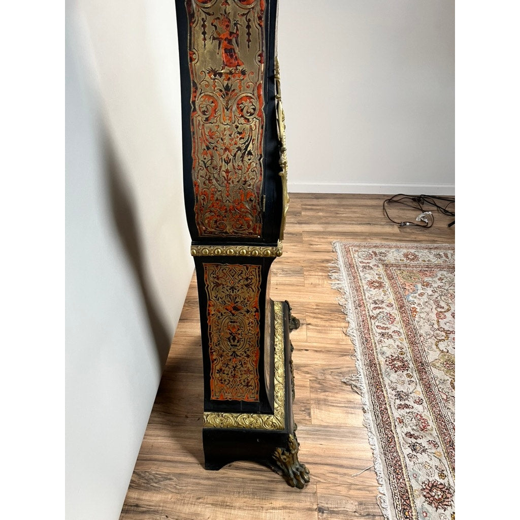 Side view of a Monumental French Napoleon III Boulle Marquetry Floor Clock with Ormolu Mounts, circa 1865–1885, featuring gold and red detailing in fine marquetry. The clock stands on a wooden floor beside a patterned rug and white wall, with some electrical cords visible in the background.