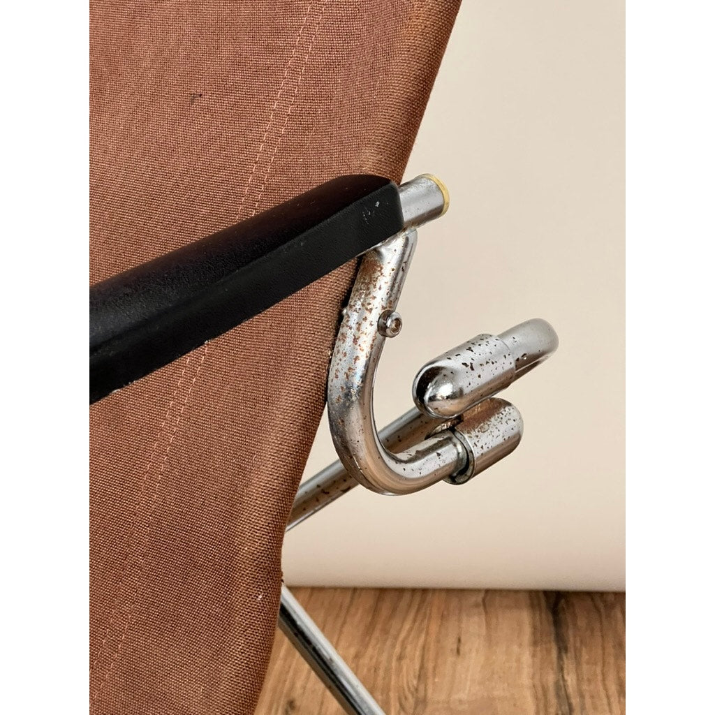 Close-up of the Vintage Uchida Z Chair, a Japanese modern chrome sling lounge chair with headrest by Uchida, featuring brown fabric upholstery and a cantilevered chrome frame that shows rust and wear on the armrest and joint. The background includes a wooden floor and light-colored wall, evoking elements of Japanese modern design.