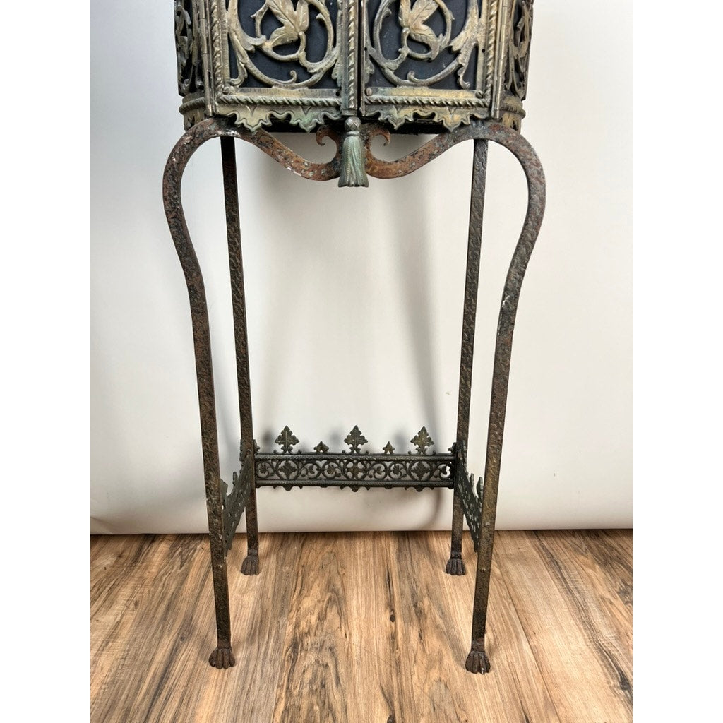 Antique Gothic Revival cast iron and brass phone stand, c. 1920 Greenwich Village, attributed to Oscar Bach or Bertram Segar, with floral motifs, four curved legs, and crossbar; displayed on a wooden floor against a plain wall.