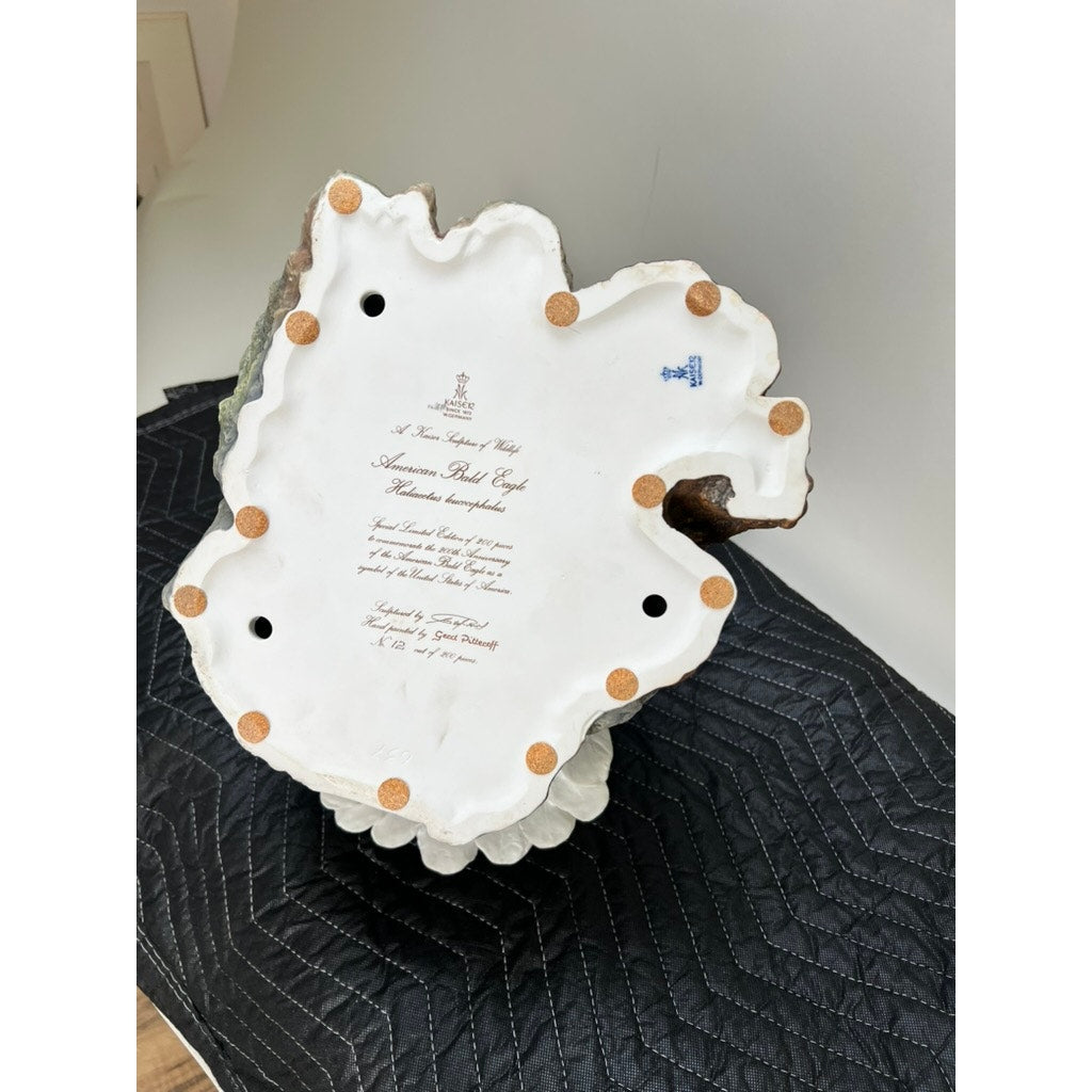 The underside of this Rare Kaiser Porcelain American Bald Eagle Sculpture (Ltd. Ed. No. 12/200, W. Germany) features a white base with brown felt pads, holes, blue and brown marks, and cursive writing authenticating the Kaiser brand.
