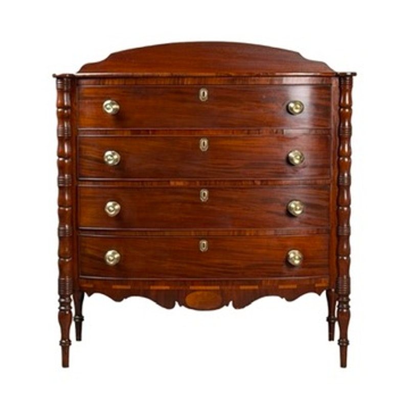 An Early 19th Century New England Federal Mahogany Bow-Front Chest of Drawers with Backsplash, dating from circa 1820–1840, this classic piece features four curved drawers with brass handles and decorative turned legs, evocative of the period’s elegant craftsmanship, displayed against a white background.