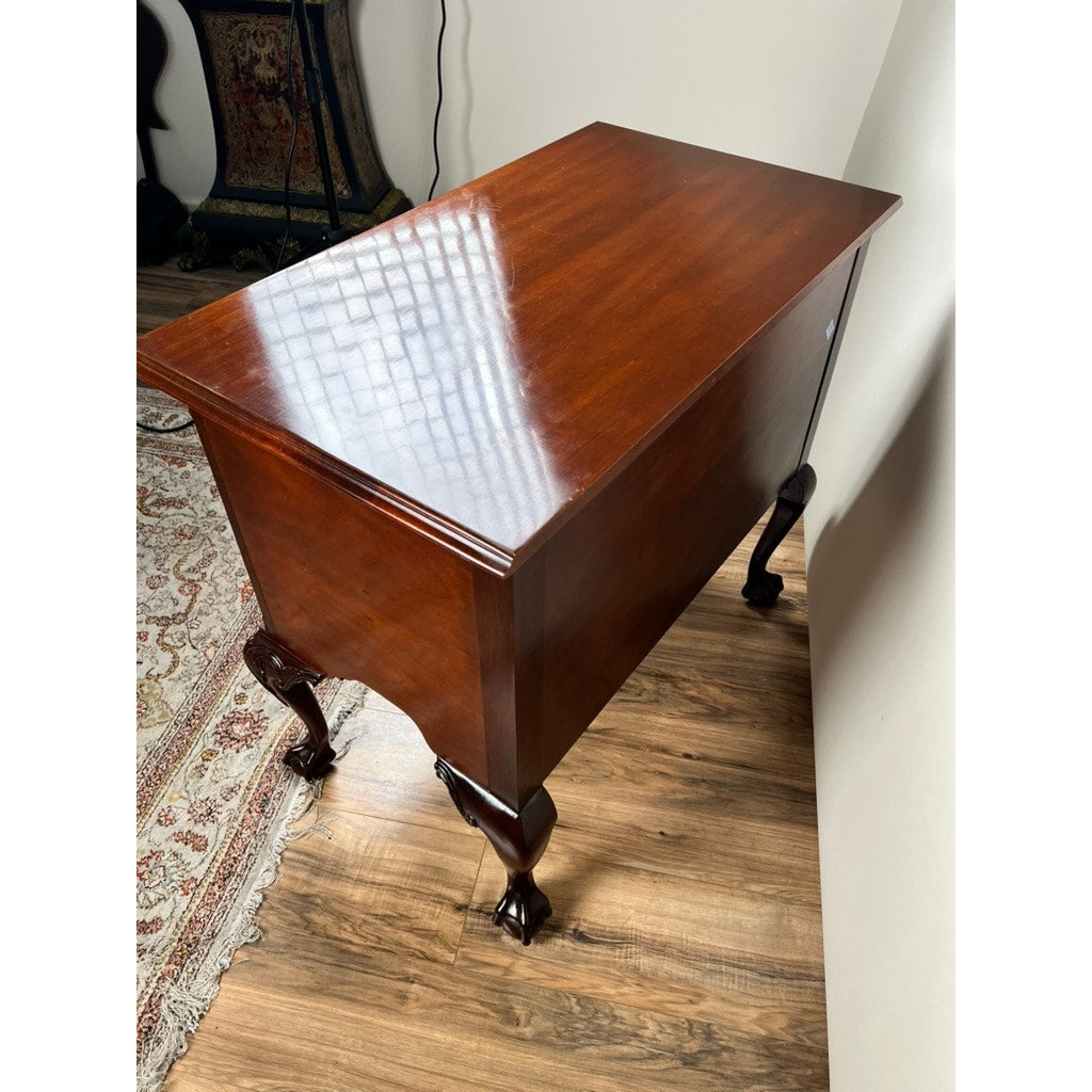 A Vintage Solid Mahogany Chippendale Style Lowboy by Councill Craftsmen stands on a wooden floor beside a patterned rug and white wall, its glossy finish reflecting window panes.