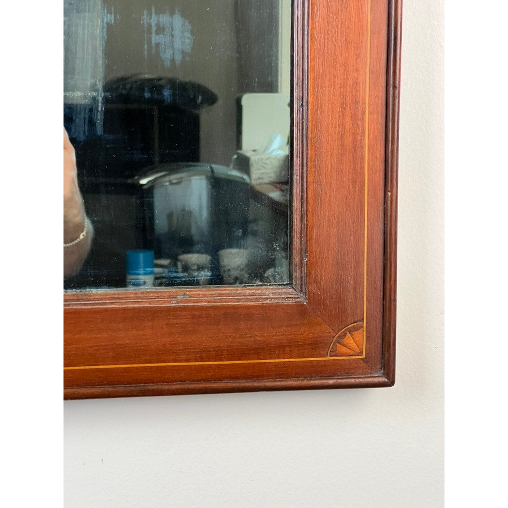 A close-up of an American Federal Mahogany Wall Mirror with Fan Inlay and Original Hand Silvered Glass, circa 1810–1825, reflects part of a room containing a coffee maker, cups, and other small items. A person's arm is partially visible on the left edge.