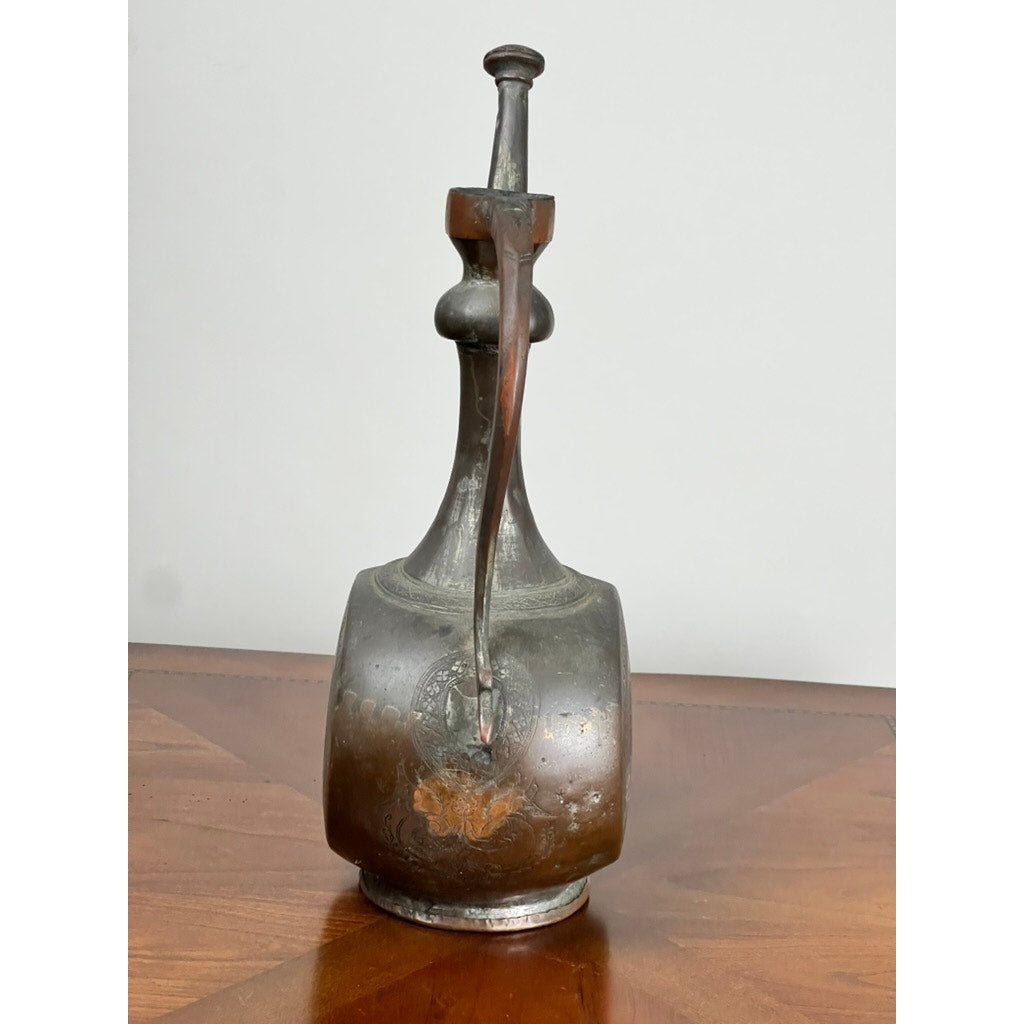 Antique Qajar Persian Copper Engraved Ewer (19th Century) with long spout, curved handle, and Islamic motifs is displayed on a wooden surface against a plain background. Brand: None/Unknown.