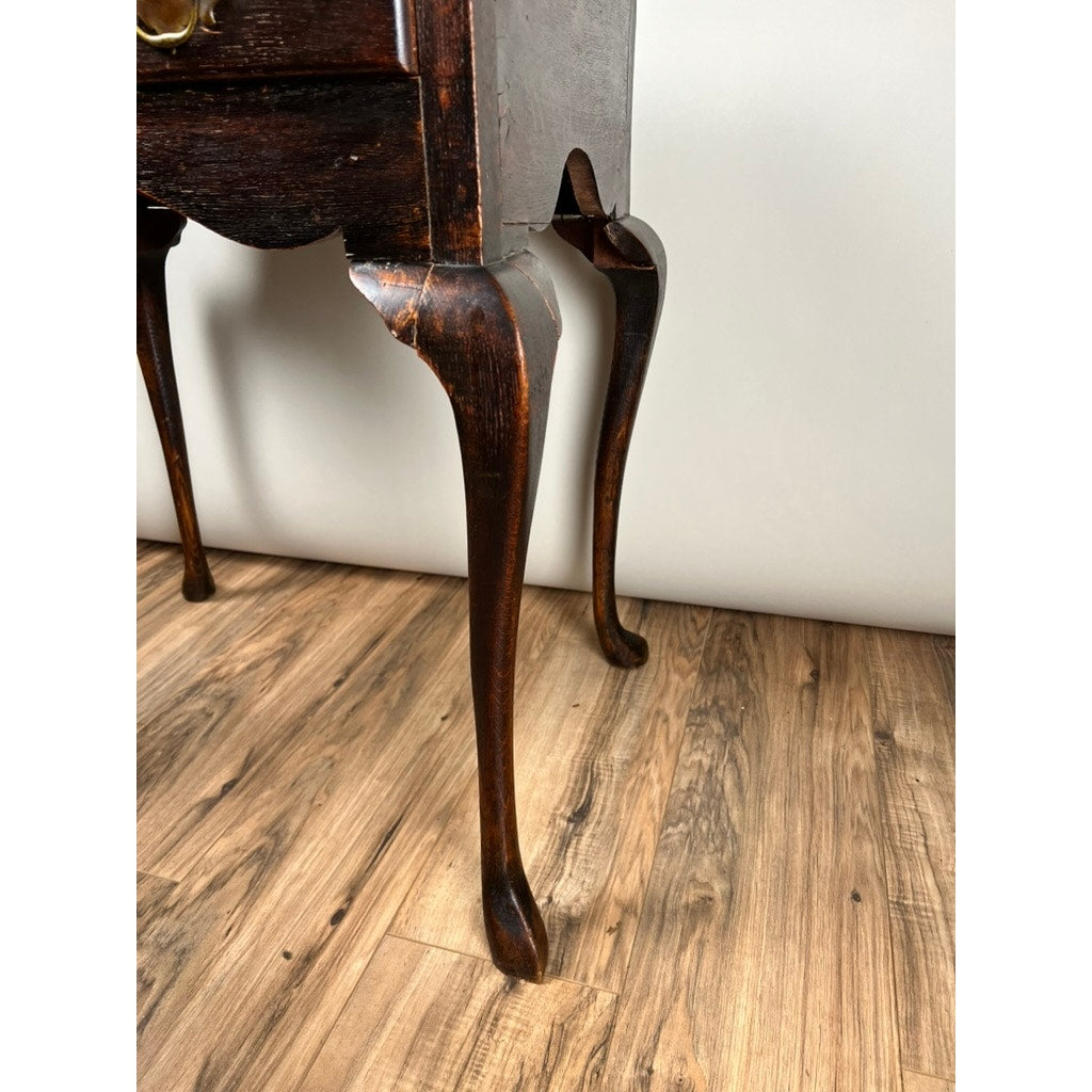 Close-up of the lower part of an Antique Queen Anne Style George III Oak One Drawer Stand (late 18th century) featuring elegant cabriole legs, set on a wood-patterned floor against a plain light-colored wall.