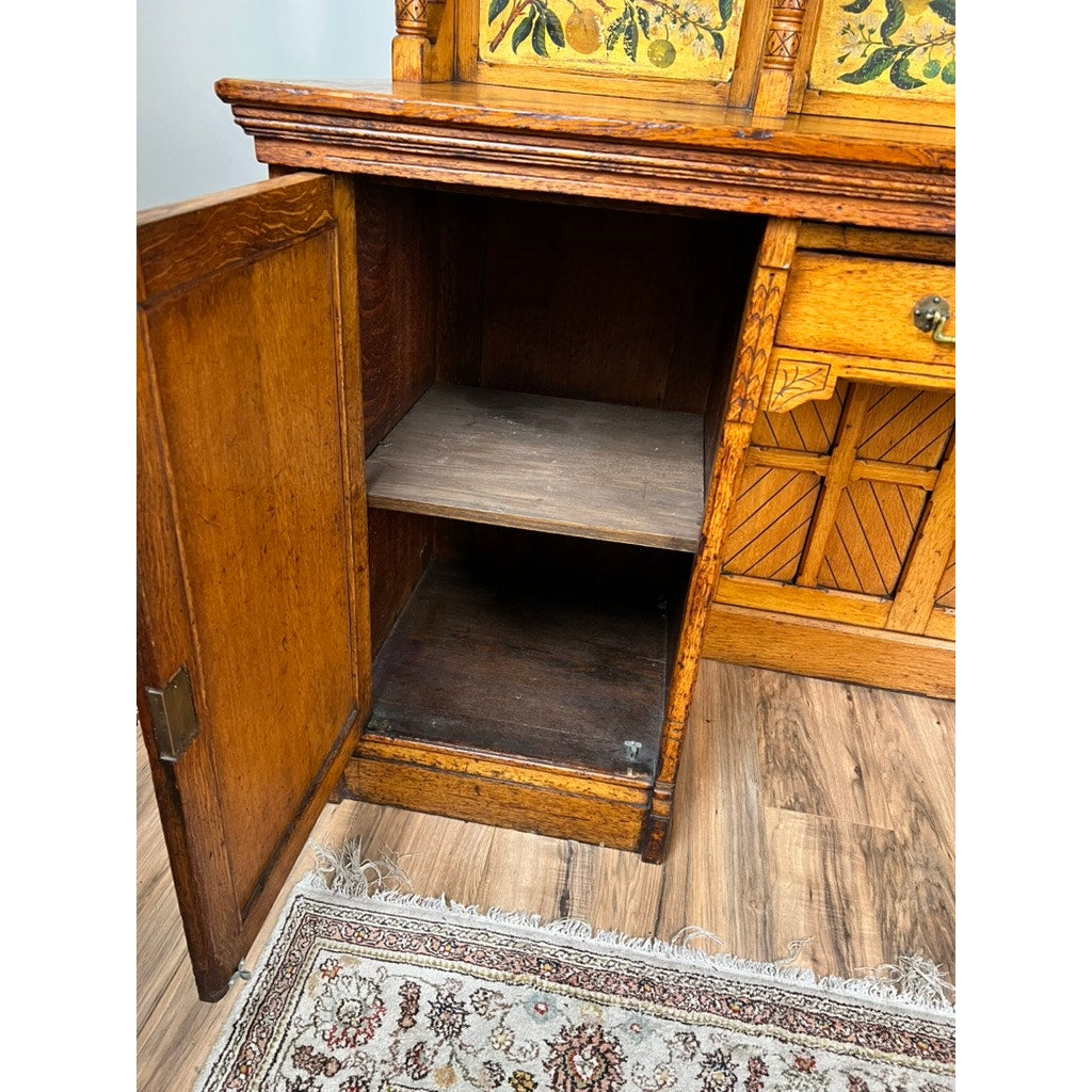 An open wooden cabinet with one shelf, part of an Antique Victorian Aesthetic Movement Oak Desk in original finish (late 19th century), featuring decorative carvings and yellow floral designs, sits on a wood floor near a patterned rug.