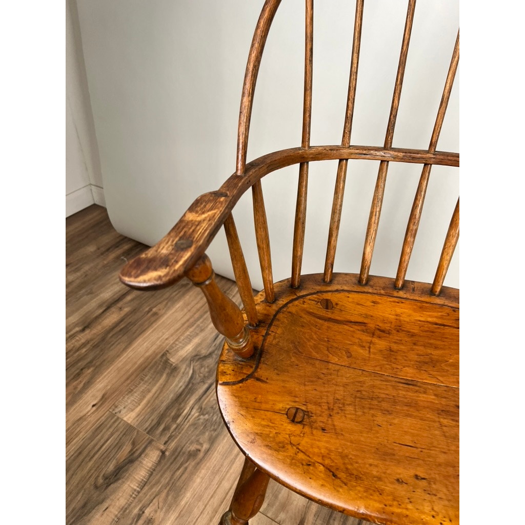 A close-up of an Antique Near Pair 18th Century Windsor Chairs, featuring early American craftsmanship with curved armrests and vertical spindles, set on a wooden floor by a plain light wall. Brand: None and/or Unknown.