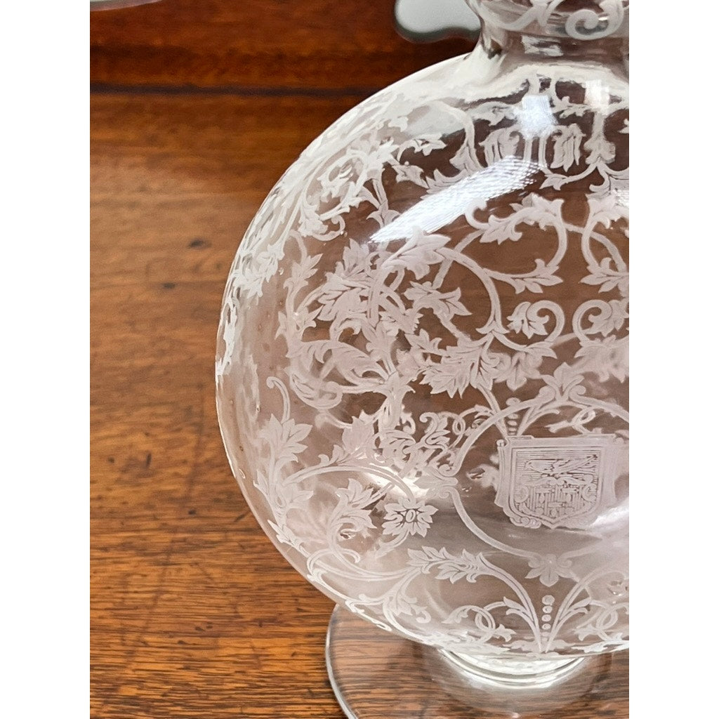 A close-up of a Vintage Baccarat Crystal Decanter in the "Michelangelo" pattern for Martell Cognac c. 1930, featuring intricate engravings and a small heraldic shield, displayed on a wooden surface.