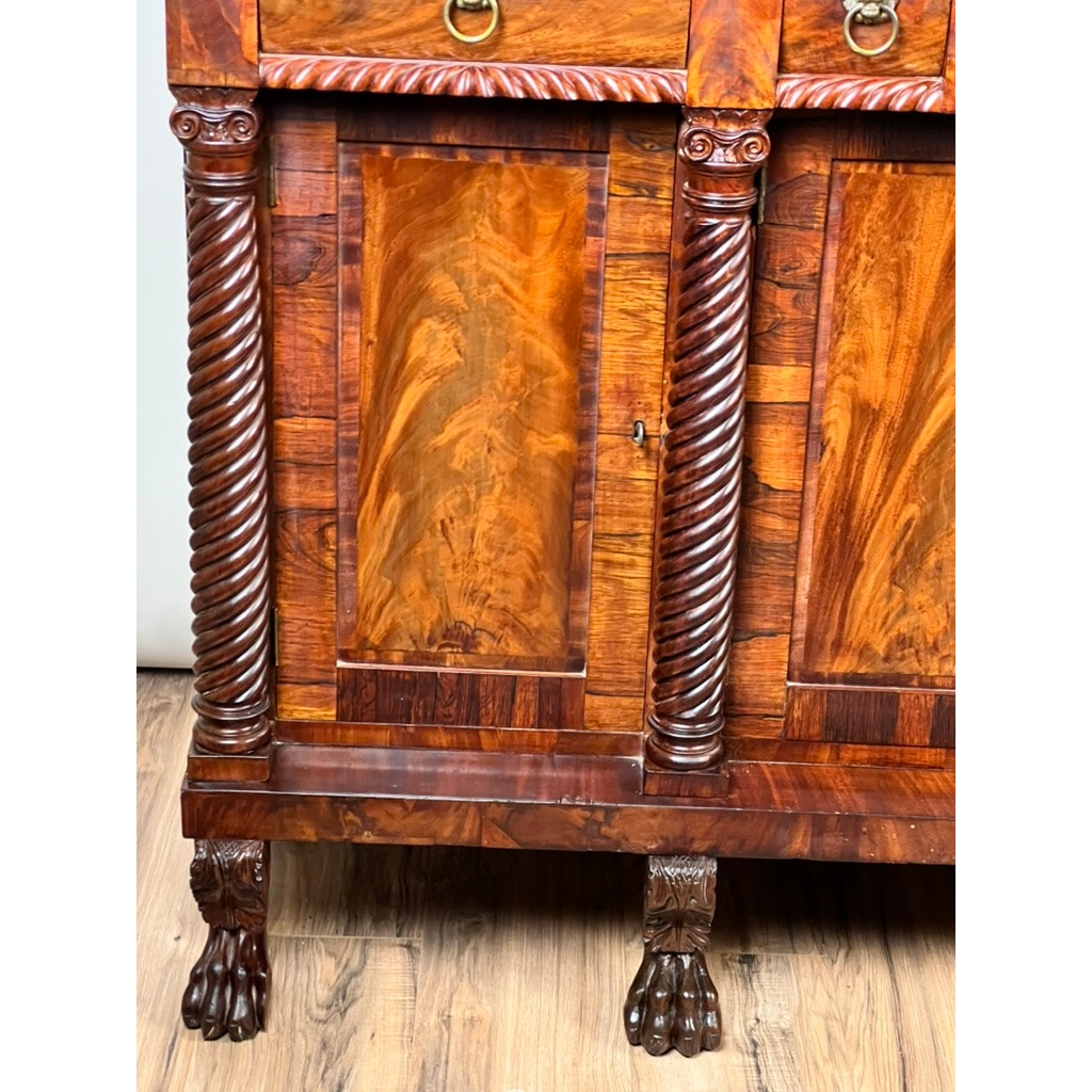Close-up of an Antique American Empire Mahogany Sideboard, c. 1840, probably Philadelphia, with rosewood edge banding, ornate carvings, twisted columns, lion paw feet, and richly grained panels set on a wooden floor.
