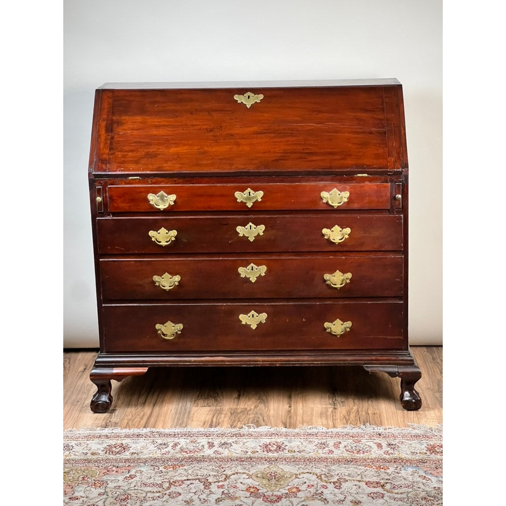 The 18th Century New England Chippendale Cherry Slant Front Desk, Circa 1770–1790 features a drop-front writing surface and four drawers accented with ornate brass handles. This solid cherry antique, crafted in the Chippendale style, stands on classic claw-and-ball feet and is showcased on a wooden floor near a patterned rug. The maker or brand is unknown.