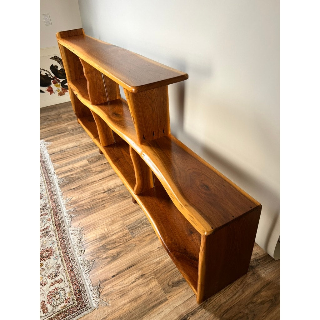The Vintage Mid-Century Modern Style Live Edge Walnut Bookshelf, featuring a wavy design and multiple shelves, stands on a wood floor beside a patterned rug.
