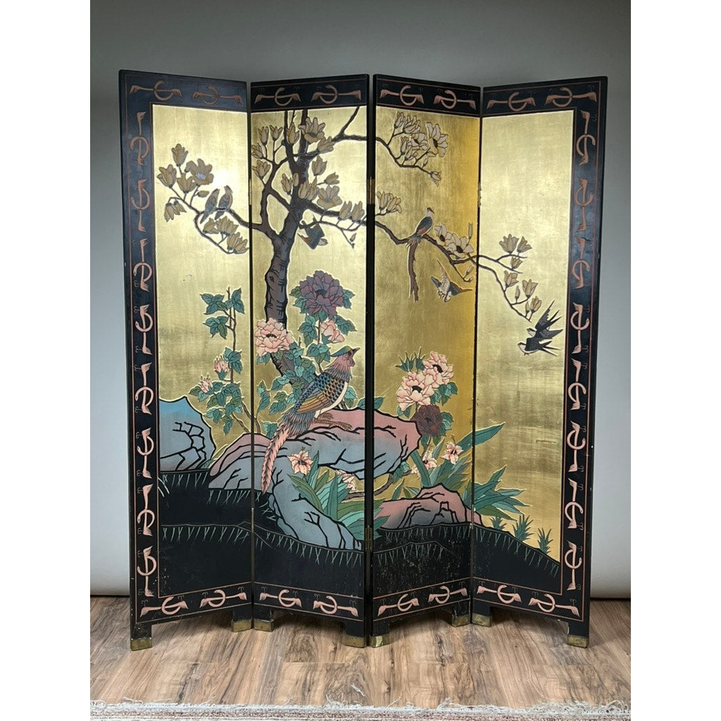 The Vintage Asian Black Lacquer Coromandel Room Screen is a decorative four-panel divider with a gold background, painted birds, flowers, rocks, and a tree. It stands on a wooden floor against a plain wall. Brand: None/Unknown.