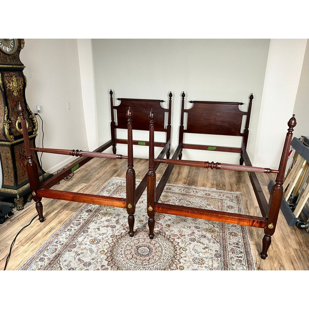 A bright room features a Vintage Pair Centennial Solid Mahogany Twin Four Poster Beds c. 1940 with tall posts and dark finishes on a patterned rug over wood flooring; an ornate clock stands in the left corner.