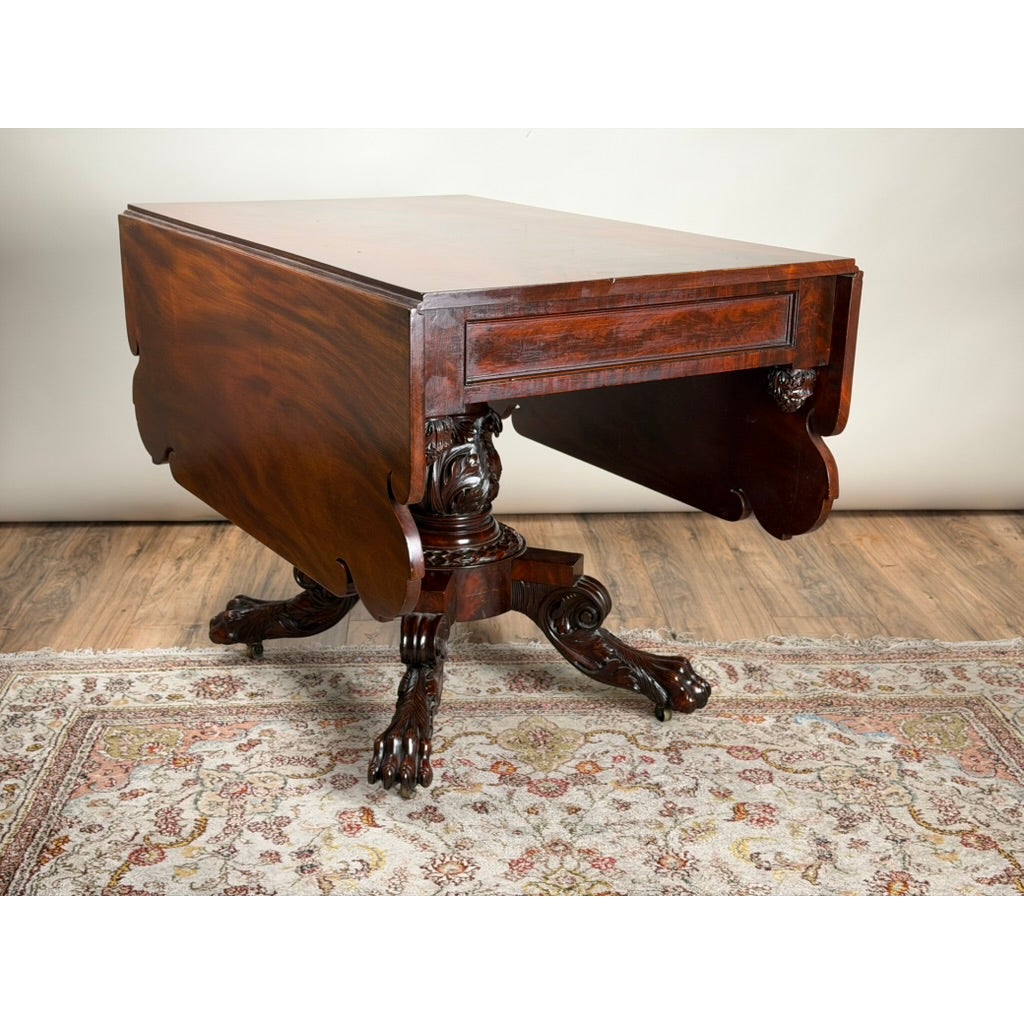 American Classical Carved Mahogany Drop-Leaf Breakfast Table, c. 1825–1840, featuring a central carved pedestal base and claw-and-ball feet.
