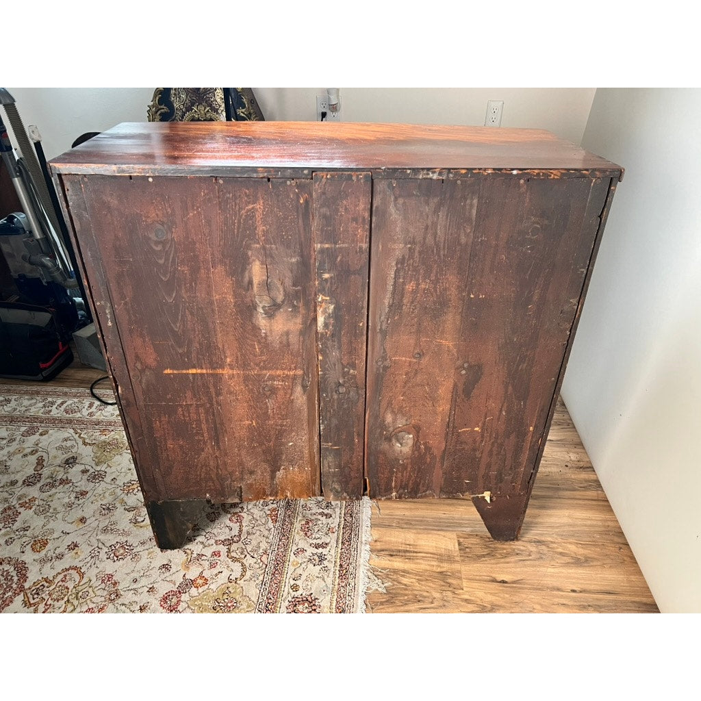 An Antique George III Mahogany Bowfront Chest on French Feet (late 18th century, brand unknown) stands on a wood floor by a patterned rug, showing visible scratches, scuff marks, and damaged bottom edges.