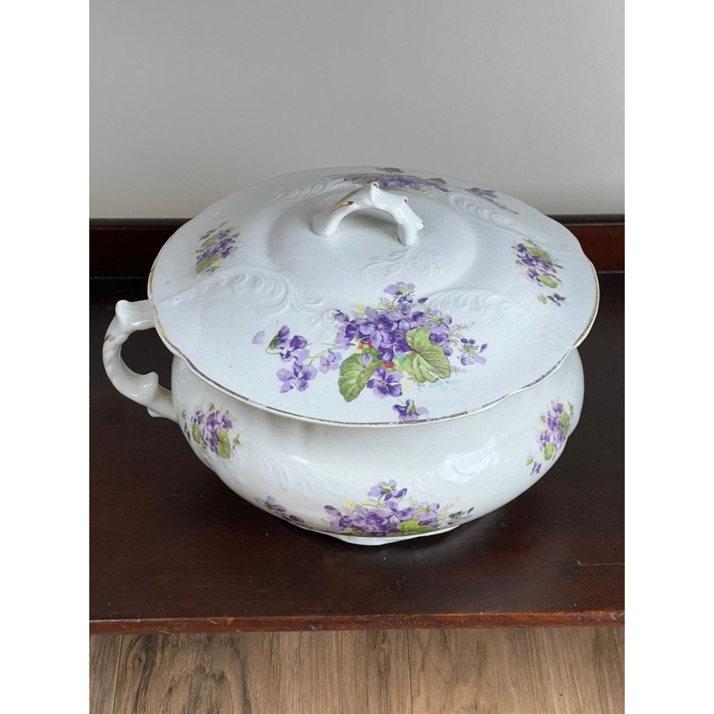 An Antique Victorian Porcelain Wash Stand Set by Leland, late 19th century, features purple violet and green leaf motifs on white porcelain. It includes a lidded tureen with a curved handle, resting elegantly on its walnut stand.
