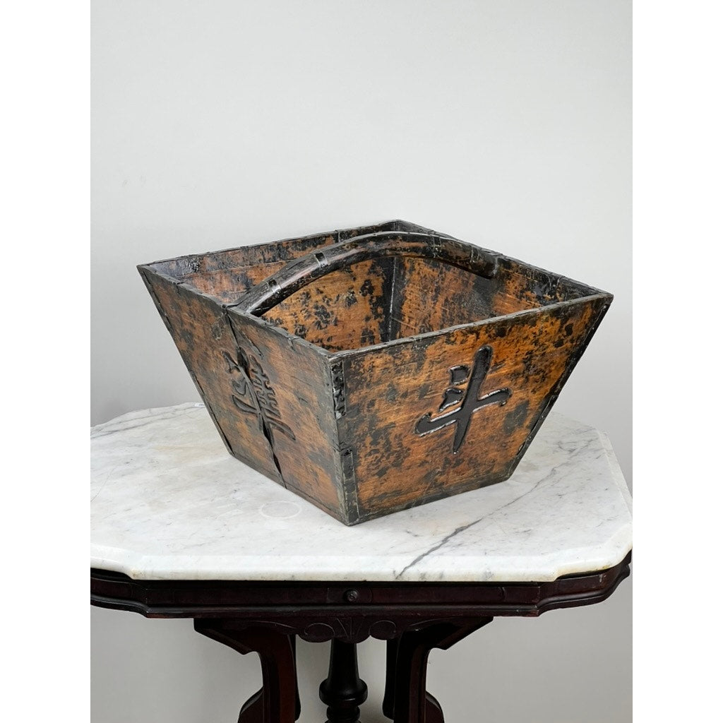 An Antique Chinese Elm Dou Rice Measure, likely from Shanxi and dating to the mid-19th century, sits atop a white marble-topped wooden table against a light gray wall; its rustic square form features engraved Asian characters.